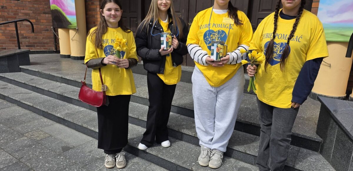 Wolontariusze ze szkoły stoją przed budynkiem i trzymają żonkile oraz puszki podczas akcji charytatywnej na rzecz hospicjum.