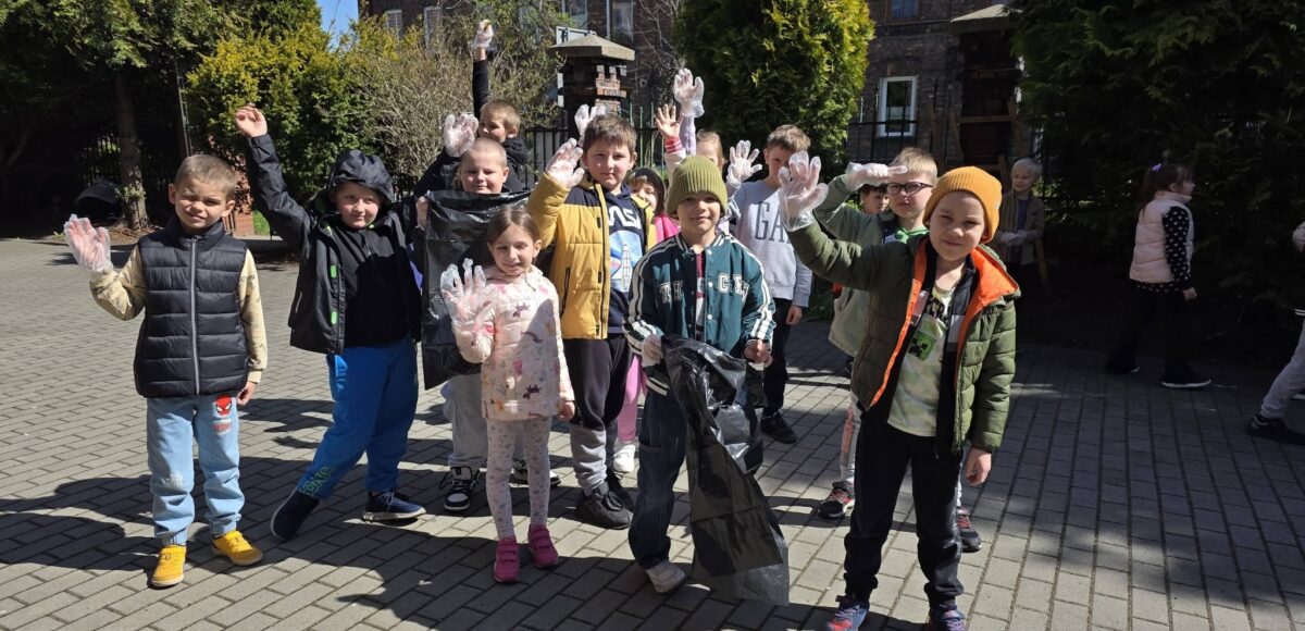 Uczniowie sprzątają teren wokół szkoły podczas obchodów Dnia Ziemi, trzymając worki i rękawice ochronne.