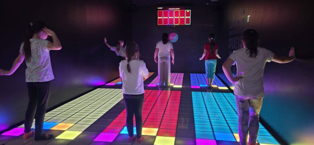 Uczniowie podczas zabawy na interaktywnej, podświetlanej podłodze w Pixel XL, biorą udział w grze ruchowej.