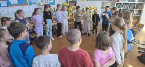 Uczniowie klasy 1–2 stoją w kręgu w sali lekcyjnej i biorą udział w zajęciach integracyjnych w ramach programu „Cukierki”.