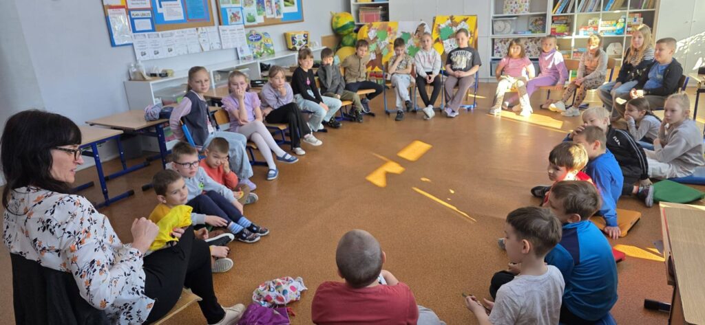 Uczniowie klas 1–2 siedzą w kręgu w sali lekcyjnej i uczestniczą w zajęciach profilaktycznych programu „Cukierki”, prowadzonych przez nauczyciela.