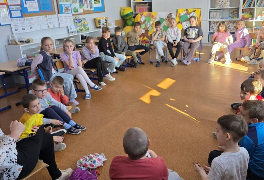 Uczniowie klas 1–2 siedzą w kręgu w sali lekcyjnej i uczestniczą w zajęciach profilaktycznych programu „Cukierki”, prowadzonych przez nauczyciela.