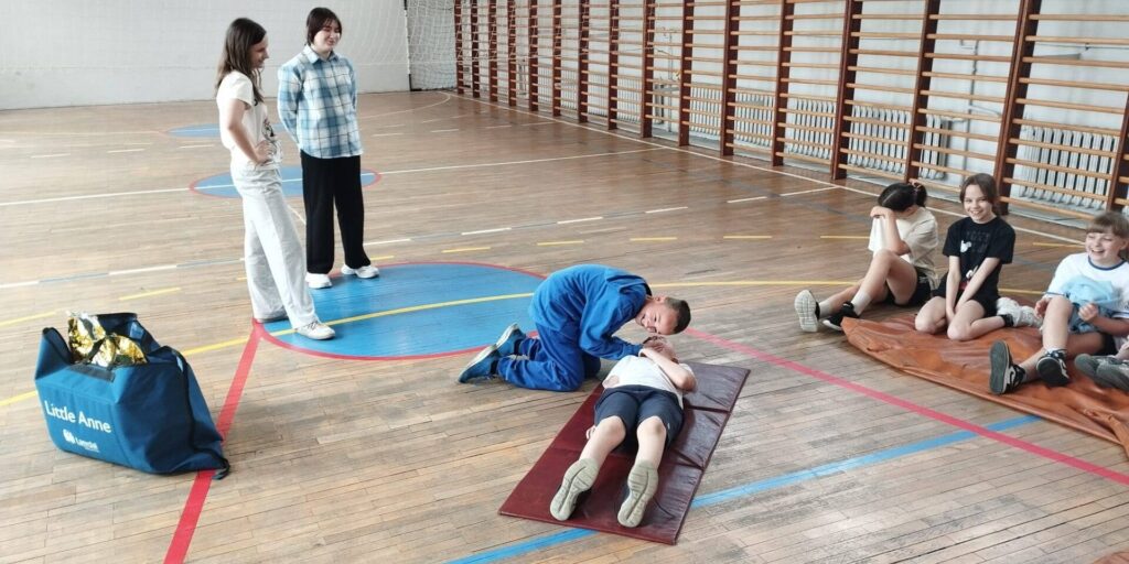 Uczniowie podczas zajęć z pierwszej pomocy na sali gimnastycznej ćwiczą prawidłowe udzielanie pomocy przedmedycznej.