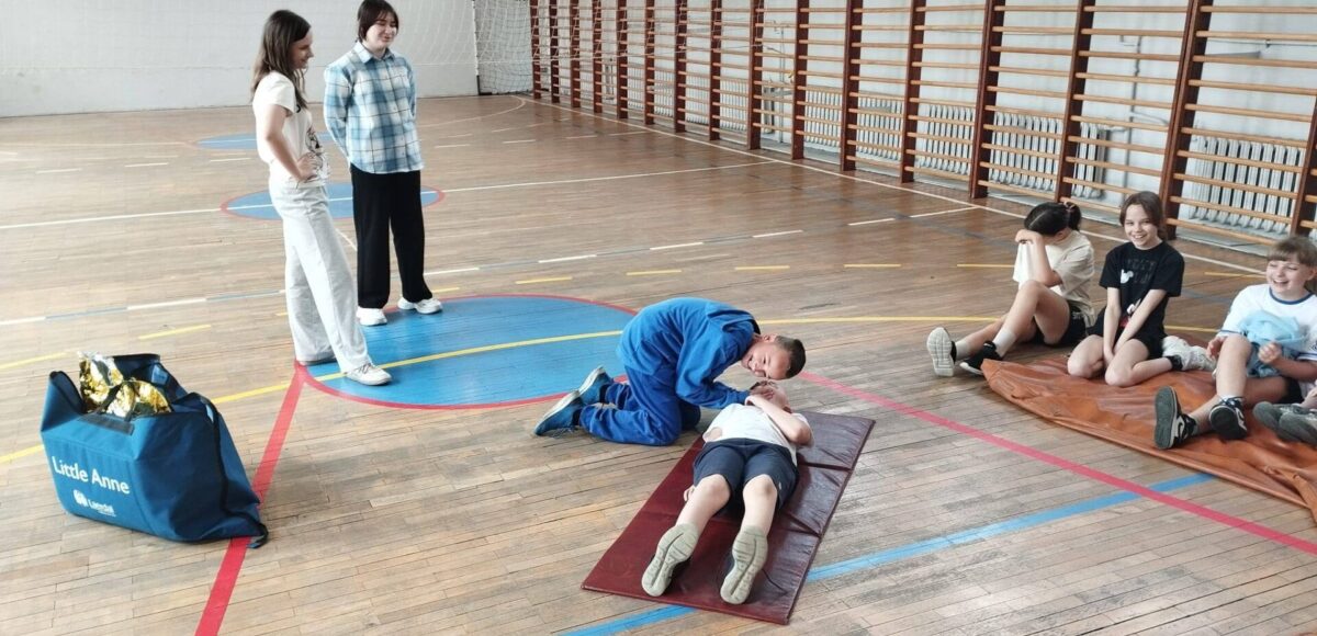 Uczniowie podczas zajęć z pierwszej pomocy na sali gimnastycznej ćwiczą prawidłowe udzielanie pomocy przedmedycznej.