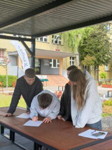 Uczniowie podczas konkursu „InterGeniusze” rozwiązują zadania przy stoliku na terenie szkoły.