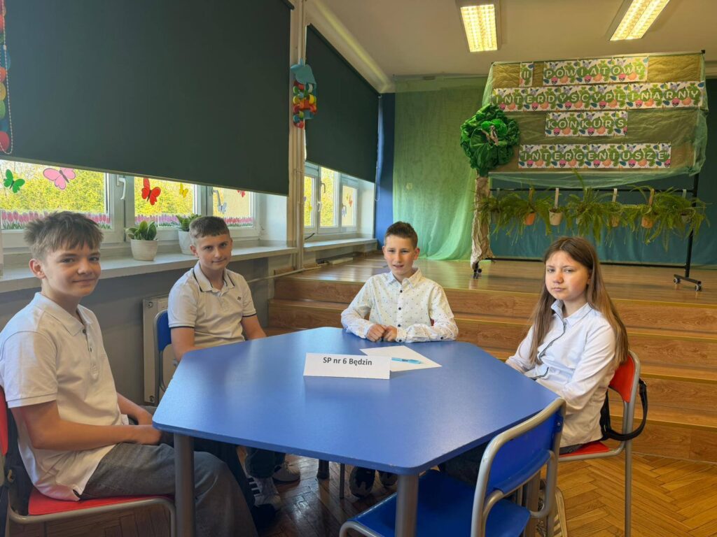 Uczniowie naszej szkoły podczas Powiatowego Konkursu Interdyscyplinarnego „InterGeniusze”, siedzą przy stoliku konkursowym.