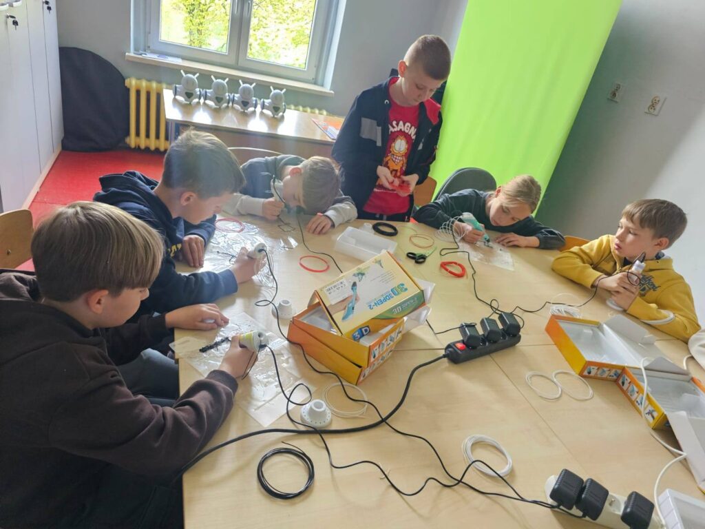 Uczniowie klasy III podczas zajęć w Laboratorium Przyszłości pracują z długopisami 3D przy wspólnym stole.