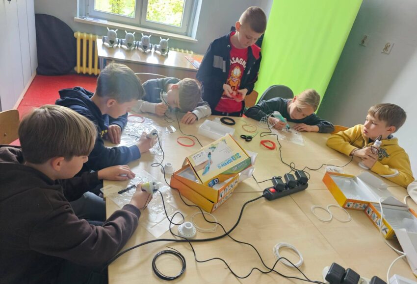 Uczniowie klasy III podczas zajęć w Laboratorium Przyszłości pracują z długopisami 3D przy wspólnym stole.