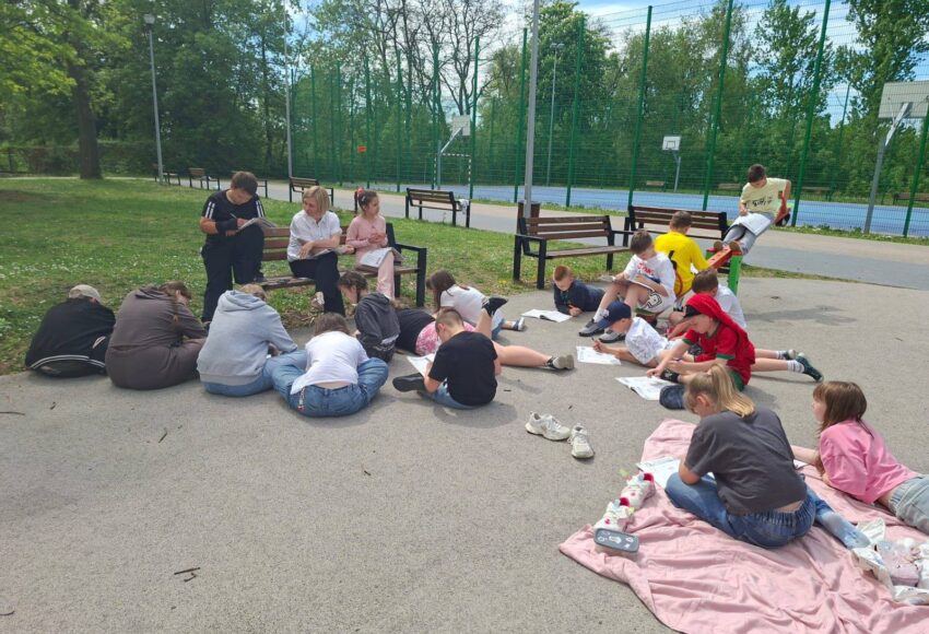 Uczniowie klasy IV a podczas zajęć outdoor learningu na terenie szkoły, pracujący w grupach na szkolnym boisku podczas lekcji języka polskiego i języka angielskiego.