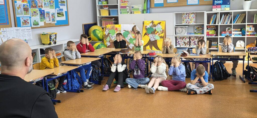 Uczniowie klas I–IV podczas warsztatów „Miej obraz osoby niewidomej”. Dzieci siedzą w sali lekcyjnej z zasłoniętymi oczami, uczestnicząc w ćwiczeniach pomagających zrozumieć codzienne wyzwania osób niewidomych.