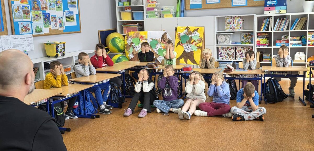 Uczniowie klas I–IV podczas warsztatów „Miej obraz osoby niewidomej”. Dzieci siedzą w sali lekcyjnej z zasłoniętymi oczami, uczestnicząc w ćwiczeniach pomagających zrozumieć codzienne wyzwania osób niewidomych.