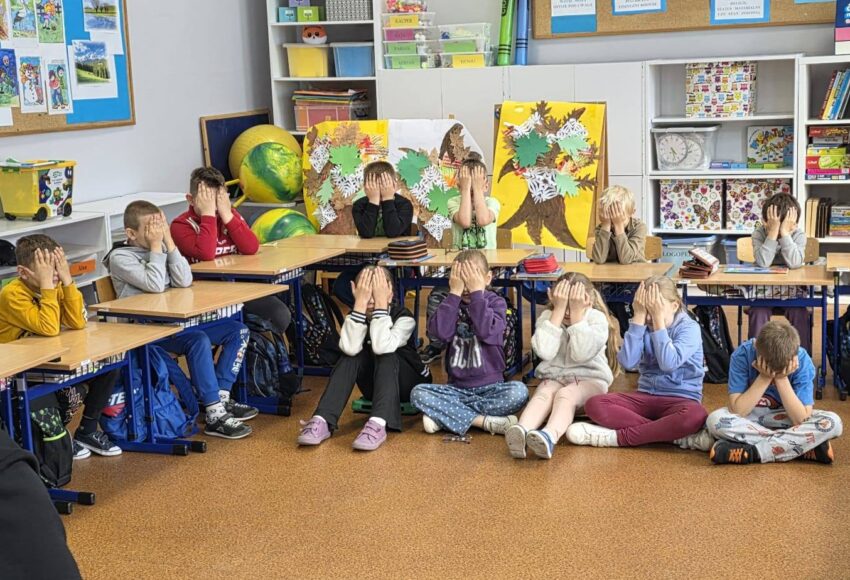 Uczniowie klas I–IV podczas warsztatów „Miej obraz osoby niewidomej”. Dzieci siedzą w sali lekcyjnej z zasłoniętymi oczami, uczestnicząc w ćwiczeniach pomagających zrozumieć codzienne wyzwania osób niewidomych.