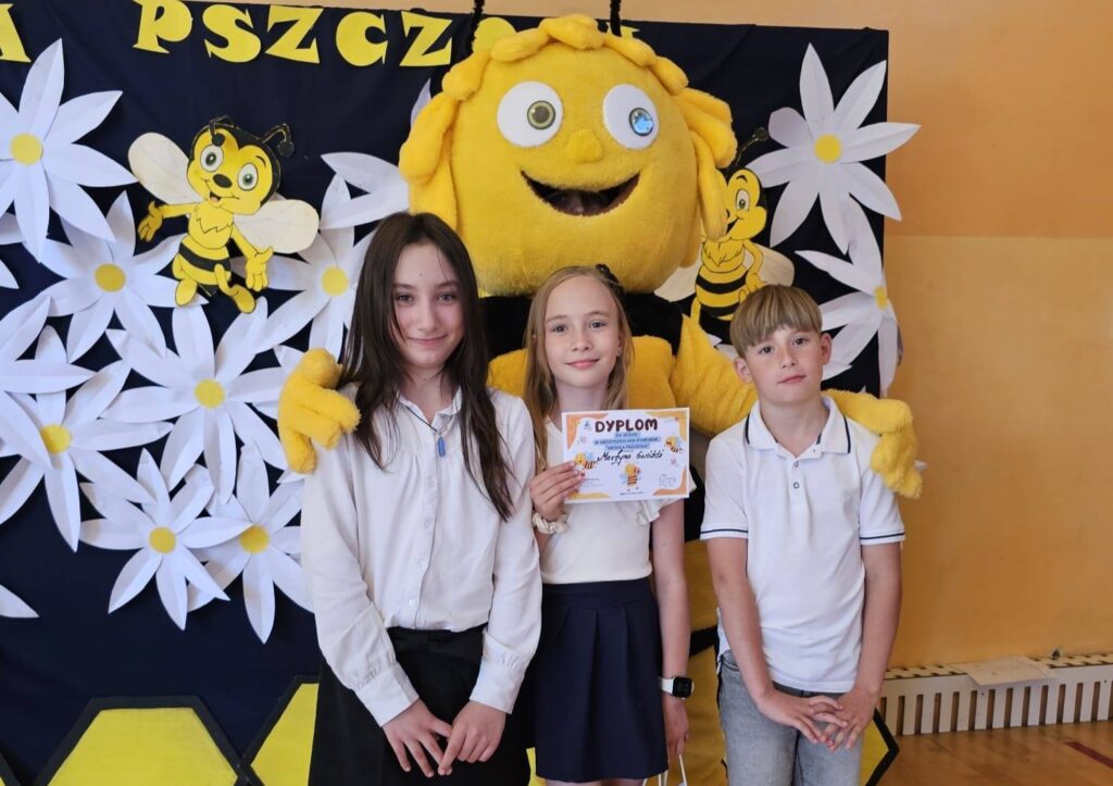 Reprezentanci klasy III pozują do zdjęcia z maskotką pszczoły po konkursie „Wesoła pszczoła”. Uczennica prezentuje dyplom zdobyty podczas wydarzenia promującego wiedzę przyrodniczą i postawy proekologiczne.