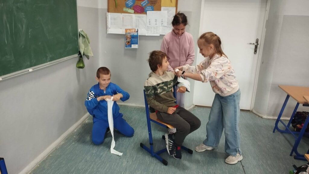 Uczniowie podczas zajęć projektu „Na ratunek” ćwiczą udzielanie pierwszej pomocy – bandażowanie i usztywnianie ręki po urazach takich jak złamania, skręcenia i zwichnięcia.