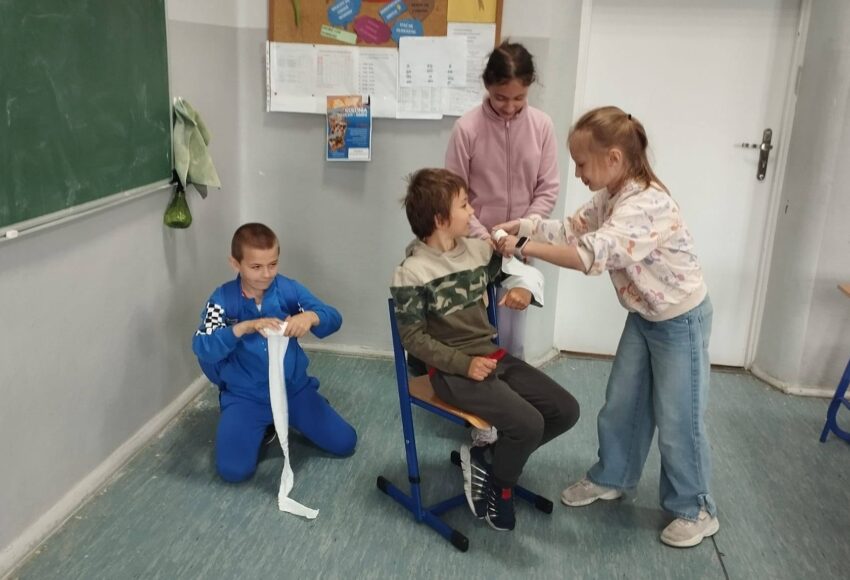 Uczniowie podczas zajęć projektu „Na ratunek” ćwiczą udzielanie pierwszej pomocy – bandażowanie i usztywnianie ręki po urazach takich jak złamania, skręcenia i zwichnięcia.