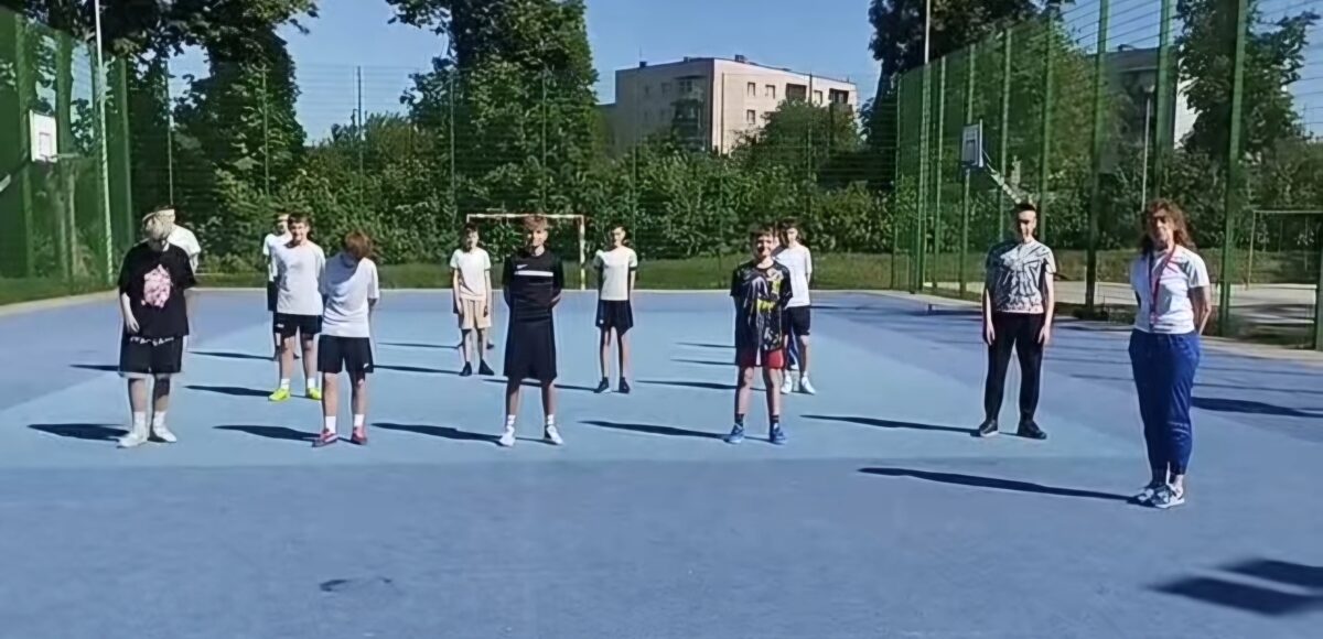Uczniowie i nauczyciele naszej szkoły podczas akcji charytatywnej „#10pompek dla Milanka” na szkolnym boisku. Uczestnicy przygotowują się do wykonania sportowego wyzwania wspierającego zbiórkę dla chorego chłopca.