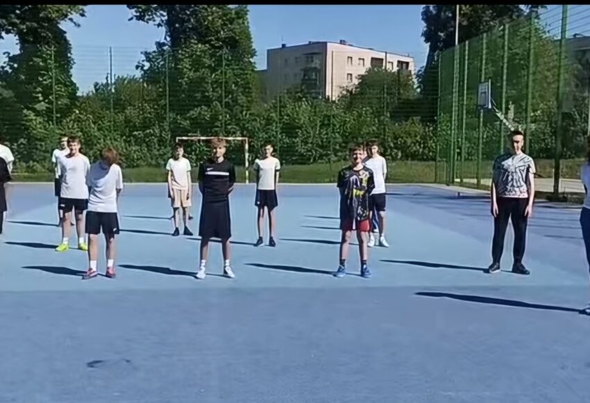 Uczniowie i nauczyciele naszej szkoły podczas akcji charytatywnej „#10pompek dla Milanka” na szkolnym boisku. Uczestnicy przygotowują się do wykonania sportowego wyzwania wspierającego zbiórkę dla chorego chłopca.