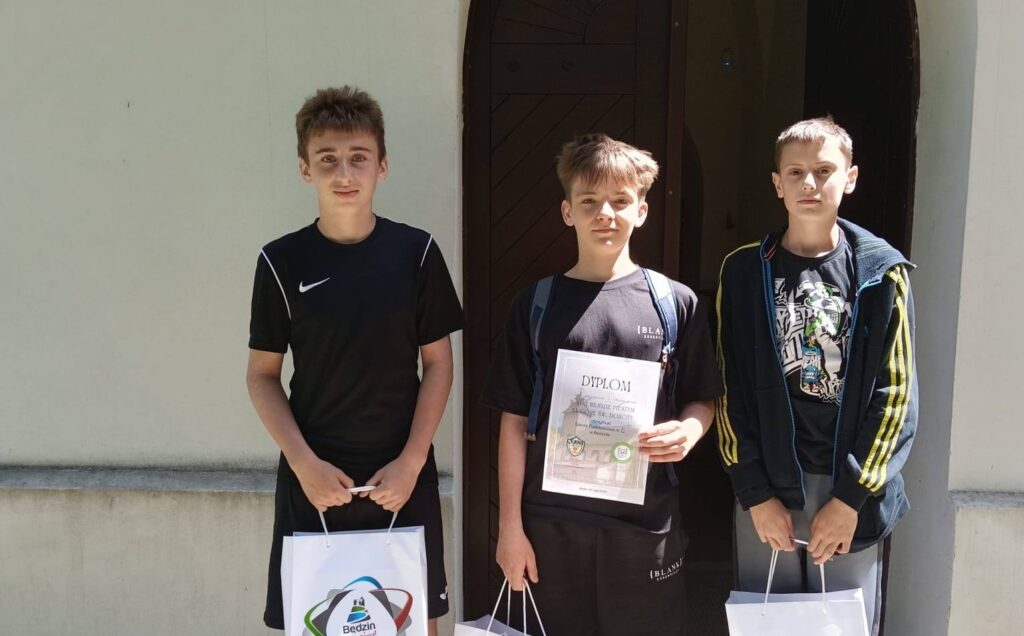 Trzej uczniowie Szkoły Podstawowej nr 6 prezentują dyplom i nagrody zdobyte za zajęcie I miejsca podczas XVIII Rajdu na Dorotkę. Zdjęcie wykonano przed zabytkowym kościołem pw. św. Doroty.