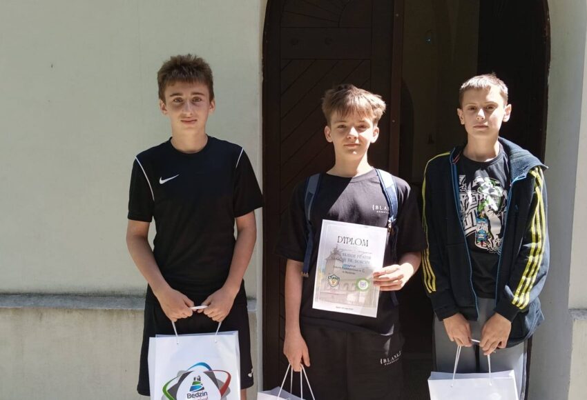 Trzej uczniowie Szkoły Podstawowej nr 6 prezentują dyplom i nagrody zdobyte za zajęcie I miejsca podczas XVIII Rajdu na Dorotkę. Zdjęcie wykonano przed zabytkowym kościołem pw. św. Doroty.