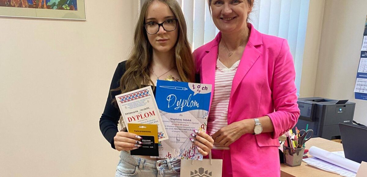 Uczennica klasy 8a Magdalena Imiołek prezentuje dyplom i nagrodę za zajęcie III miejsca w Miejskim Konkursie Ortograficznym „Mistrz Ortografii”. Obok stoi dyrektor szkoły.
