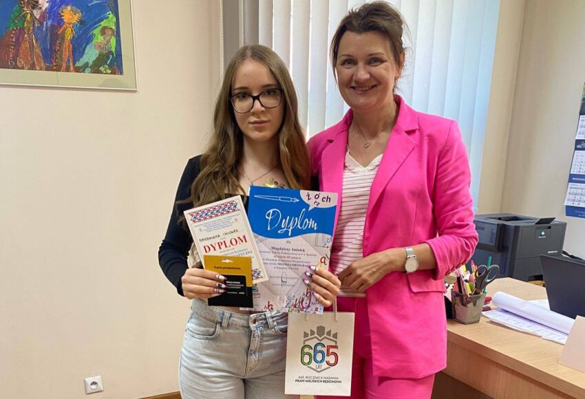 Uczennica klasy 8a Magdalena Imiołek prezentuje dyplom i nagrodę za zajęcie III miejsca w Miejskim Konkursie Ortograficznym „Mistrz Ortografii”. Obok stoi dyrektor szkoły.