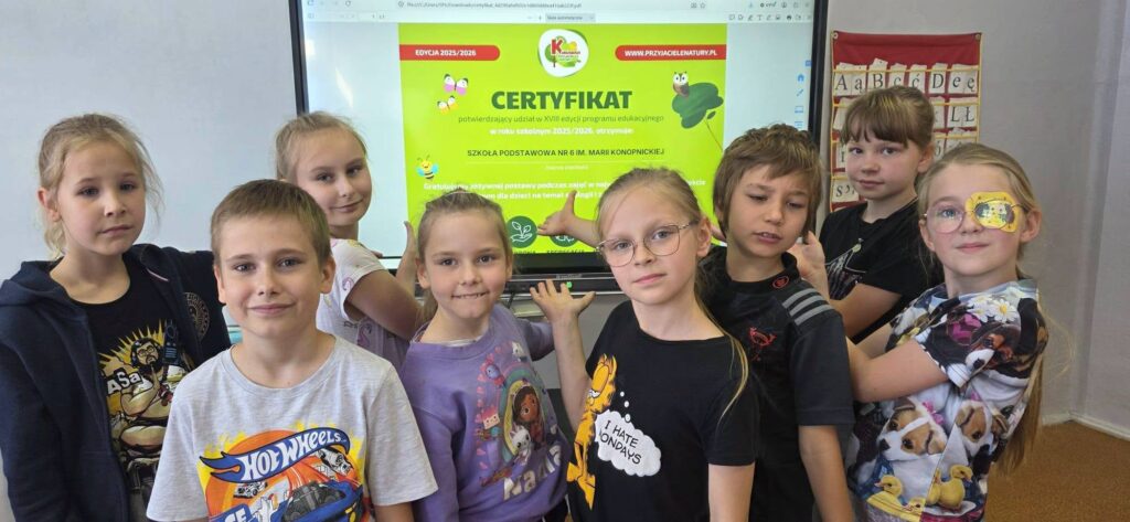 Uczniowie klas 1–2 prezentują certyfikat programu „Kubusiowi Przyjaciele Natury”, który szkoła otrzymała za udział w działaniach promujących zdrowy styl życia i edukację ekologiczną.