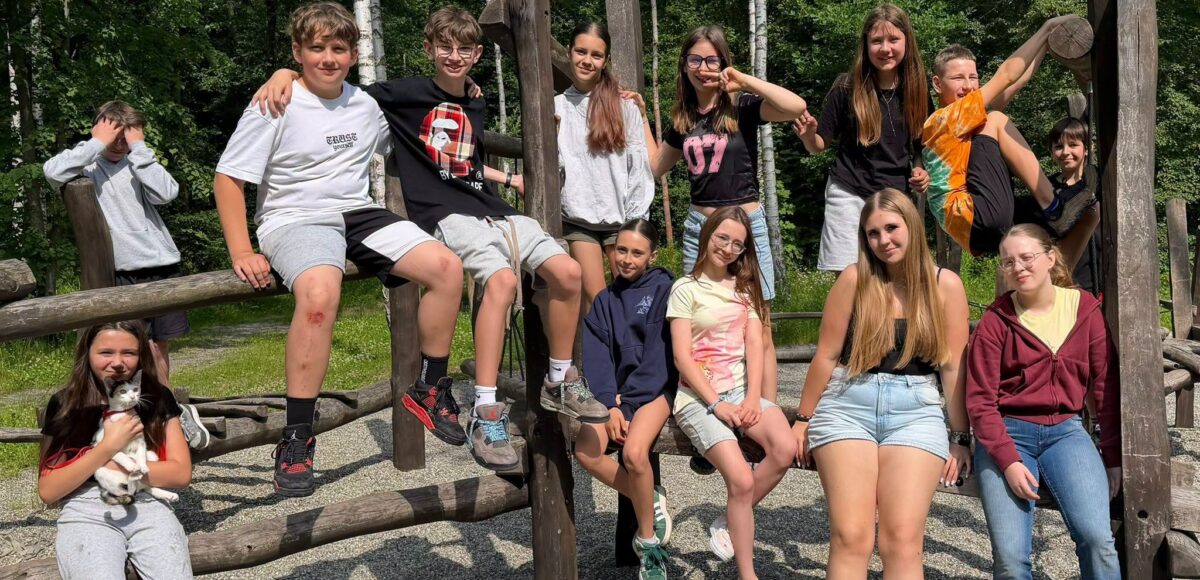 Uczniowie klasy 6 podczas integracyjnego spotkania w Parku Rozkówka pozują do wspólnego zdjęcia na drewnianej konstrukcji placu zabaw.
