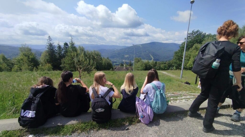 Uczniowie klas siódmych odpoczywają podczas górskiej wycieczki na Równicę, podziwiając panoramę Beskidu Śląskiego.