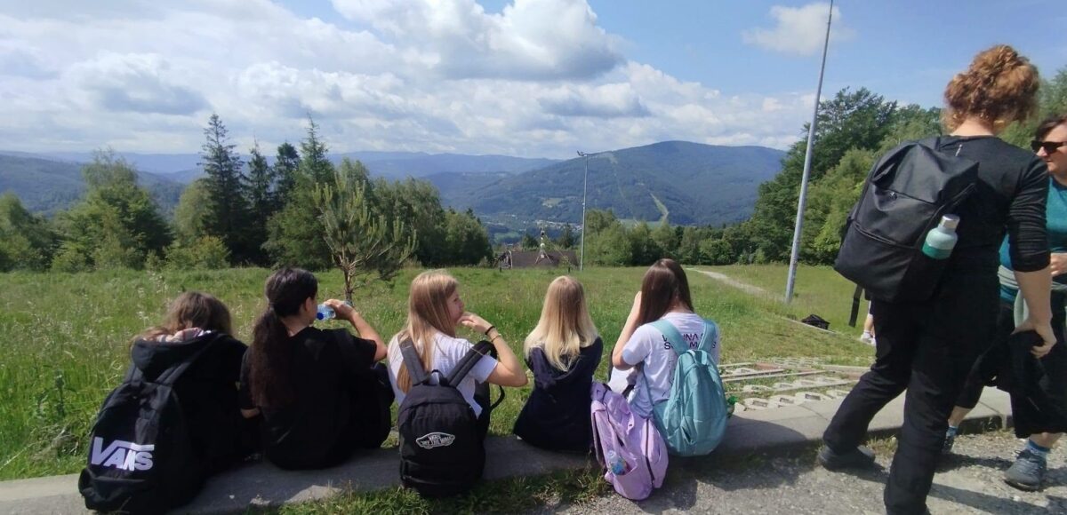 Uczniowie klas siódmych odpoczywają podczas górskiej wycieczki na Równicę, podziwiając panoramę Beskidu Śląskiego.