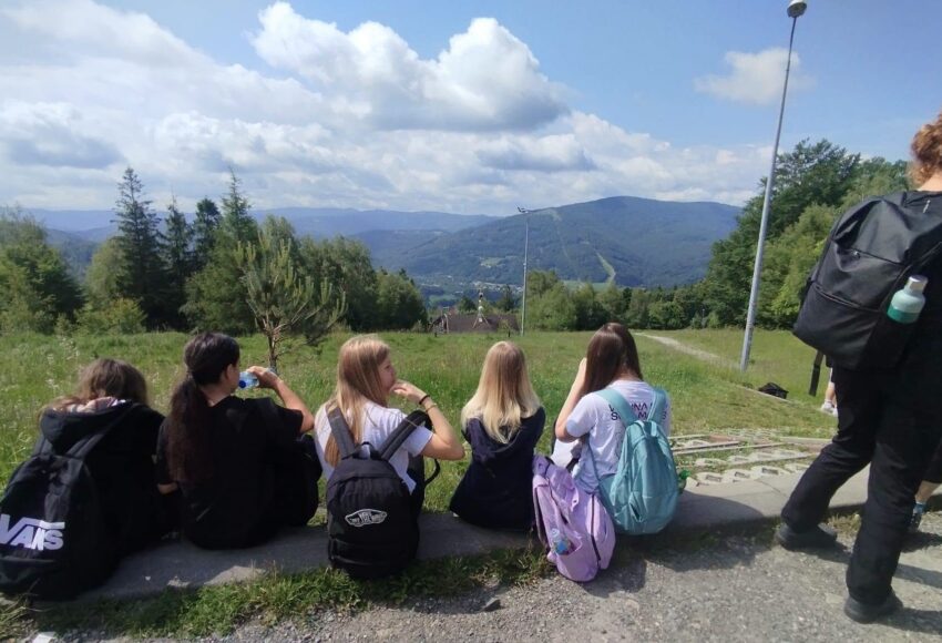 Uczniowie klas siódmych odpoczywają podczas górskiej wycieczki na Równicę, podziwiając panoramę Beskidu Śląskiego.