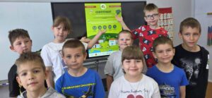 Uczniowie klas 1–2 prezentują certyfikat programu „Kubusiowi Przyjaciele Natury”, który szkoła otrzymała za udział w działaniach promujących zdrowy styl życia i edukację ekologiczną.