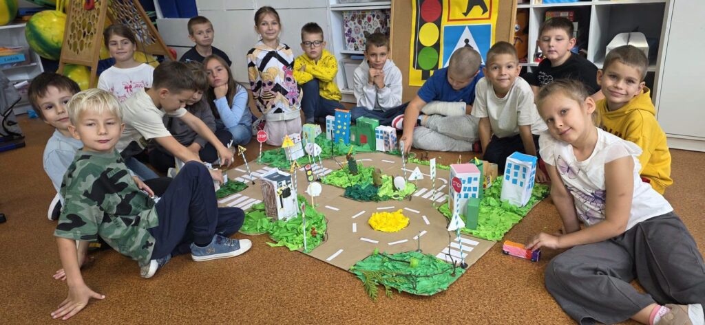 Uczniowie klasy 2 prezentują wspólnie wykonaną makietę miasta z ulicami, przejściami dla pieszych i znakami drogowymi.