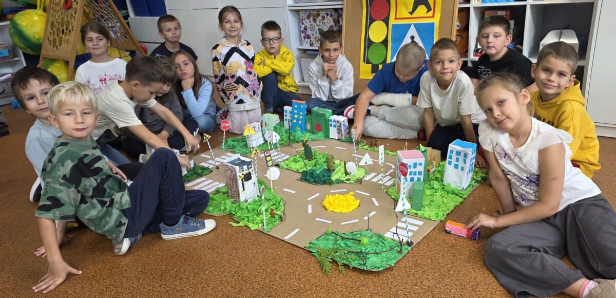 Uczniowie klasy 2 prezentują wspólnie wykonaną makietę miasta z ulicami, przejściami dla pieszych i znakami drogowymi.
