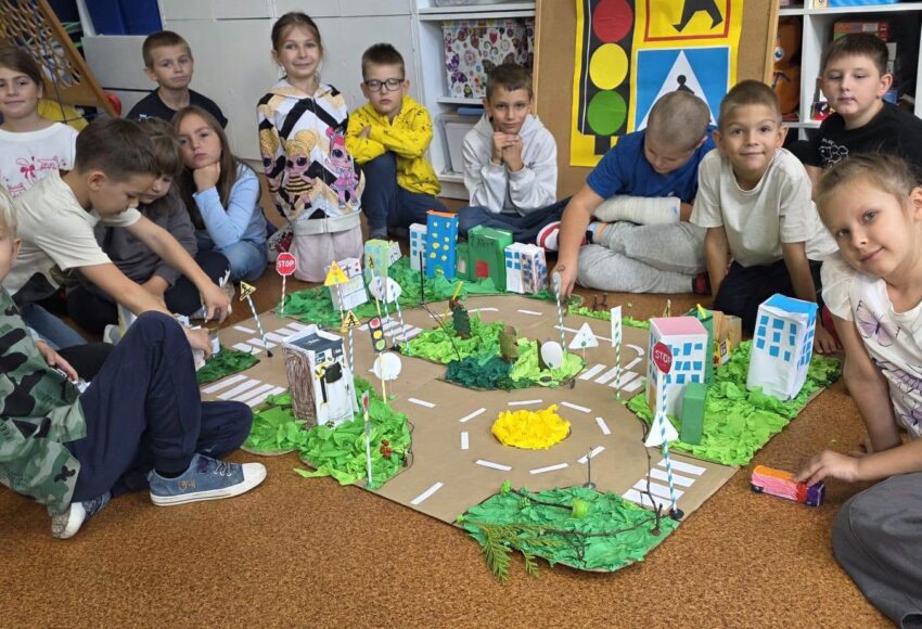 Uczniowie klasy 2 prezentują wspólnie wykonaną makietę miasta z ulicami, przejściami dla pieszych i znakami drogowymi.
