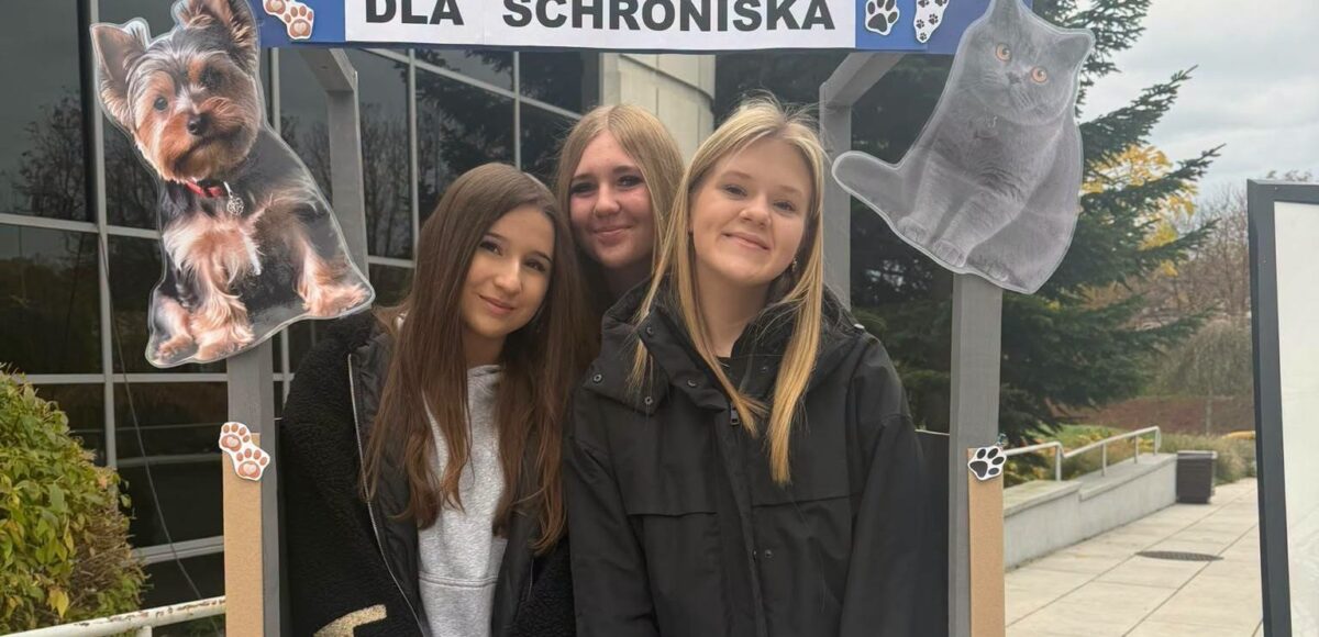 Trzy uczennice Szkoły Podstawowej nr 6 w Będzinie podczas XIV edycji akcji charytatywnej „Pełna Miska dla Schroniska”, przed dekoracyjną ramką z wizerunkami psa i kota.